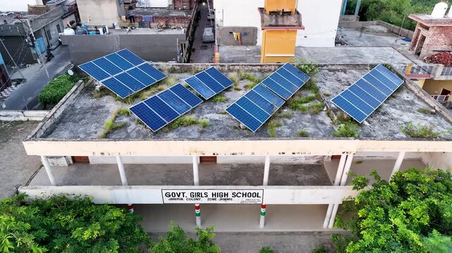 Drone pulling back to reveal a government school building powered by rooftop solar panels in an Indian town, showcasing clean renewable energy.