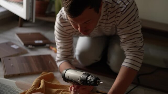 Caring father assembling new furniture on the floor, simultaneously teaching his curious infant son about a power screwdriver and involving him in the process of building a closet
