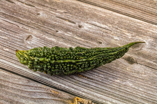 Fresh green bitter melon on weathered wooden surface, close up with natural texture and rustic background
