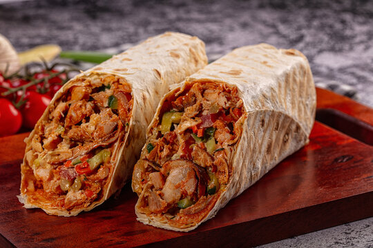 Sliced chicken wrap with vegetables and sauce on wooden board, rustic background with cherry tomatoes and garlic