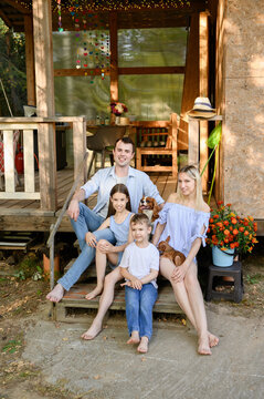 Happy family enjoying country house dacha staycation, parents with kids and dogs on rustic porch embracing cozy summer vacation, family bonding, trust and care, summer cottage vacation, relaxation.