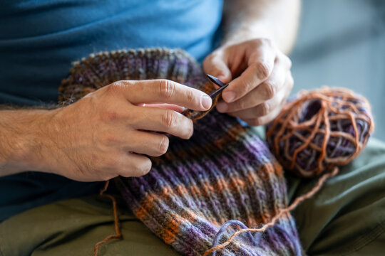 A man knitting something with colorful wool - closeup on hands and needles