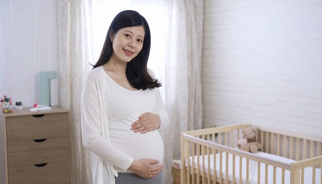 Smiling expectant mother touching pregnant belly inside modern baby nursery near white wooden crib