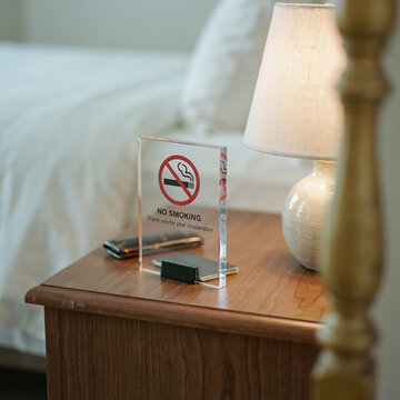 No smoking sign on hotel bedside table, acrylic warning plaque in guest room, hospitality smoke-free policy notice on wooden nightstand