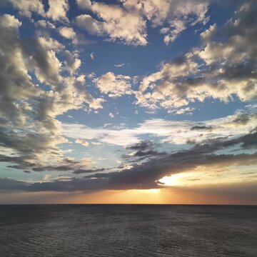 Sun sets over the ocean while clouds move across the sky. Gentle waves roll in as the day ends at the seaside.