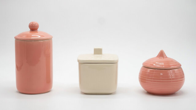 Set of three ceramic storage jars with lids in pink and cream colors on a white background