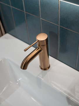 Close-up of a slim brushed copper basin mixer on a white ceramic top, handmade-look blue-green zellige tiles behind.