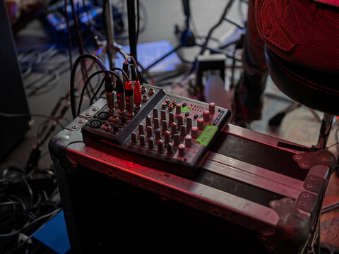 A compact analogue sound mixer with knobs, cables and labelled tape sits on a flight case at the side of the stage in red light.