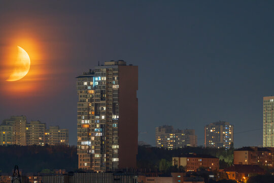 Beautiful wide view of a large orange moon rising through clouds behind city buildings at night