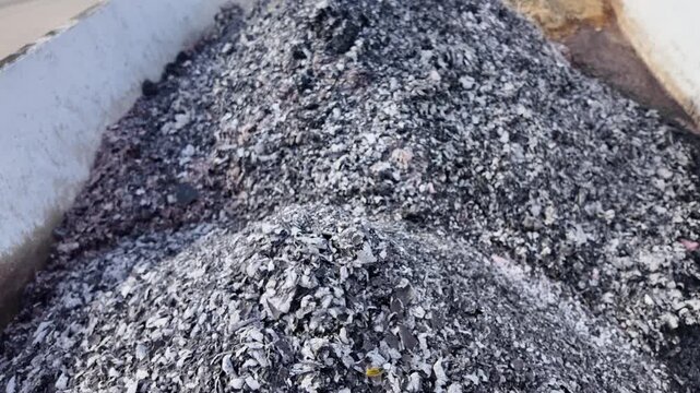 Large pile of industrial ash and burnt organic waste inside a metal container for disposal. A close up view of a heap of grey and black incinerated material stored within a white industrial bin ready 