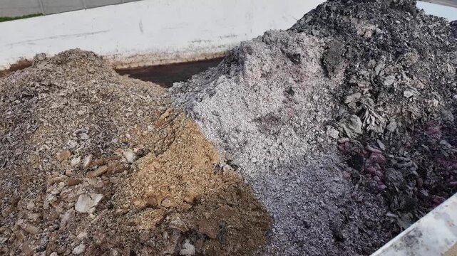 Large metal container filled with piles of industrial ash and organic waste material. A close view of a heavy duty steel skip containing mixed debris including grey ash and brown organic matter for wa