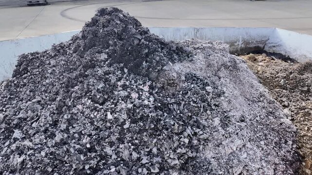 Large piles of industrial ash and organic waste stored inside a white metal container at a facility. A close view of grey powdery residue and fibrous material collected within a storage bin located on