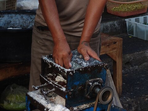 Manual coconut grating process at a busy traditional market in Yogyakarta Java Indonesian cultural street food preparation scene