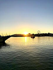 Fototapeta premium Sunset over a calm bay with a ferris wheel in the distance