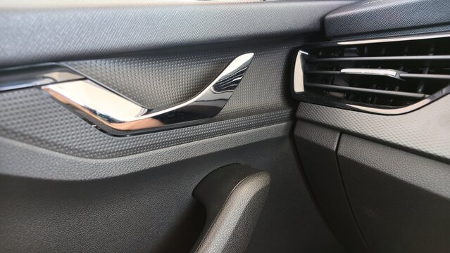 Close-up of a car interior door panel with a chrome door handle, textured trim and adjacent air vent in a modern vehicle cabin