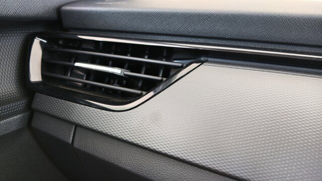 Close-up of a modern car dashboard air vent with horizontal slats, glossy black trim and textured interior panel