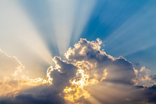Dramatic tropical sunset over the seaside, with golden sun rays breaking through layers of clouds and illuminating the sky above the calm ocean. The warm evening light creates a striking atmosphere, w