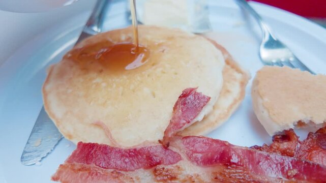 Pouring Maple Syrup on Pancakes with Crispy Bacon at Breakfast