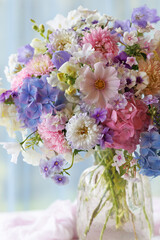 Fototapeta premium Beautiful bouquet in a vase flowers phlox, asters, hydrangeas, and bellflowers on a table, still life closeup set against a window overlooking the garden, blur, selective focus.