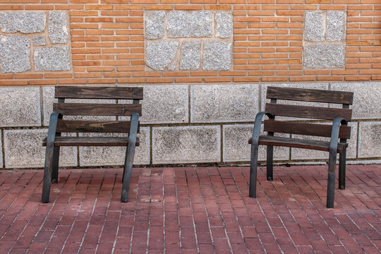 a couple of chairs on a street next to a brick and stone wall, forming part of the street furniture