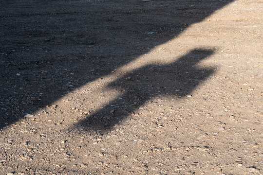 shadow of a pharmacy cross on a dirt ground