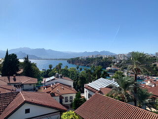 Obraz premium Panoramic view of the sea, mountains, and red-tiled roofs of Antalya’s historic old town, Turkey. Yenikapı and Kaleiçi districts. Roofs with solar panels.