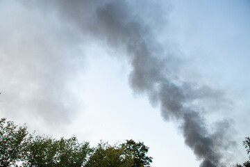 Obraz premium Thick black smoke rises above the trees after a drone attack in Ukraine. The concept of fire, missile attack, drone raid