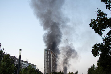 Obraz premium Thick black smoke rises from the top of an apartment building after a drone attack in Ukraine. The concept of fire, missile attack, drone raid