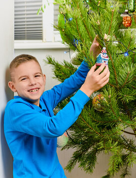 Happy boy decorating a Christmas tree with colorful ornaments and lights at home, celebrating the holiday season and enjoying a festive family tradition