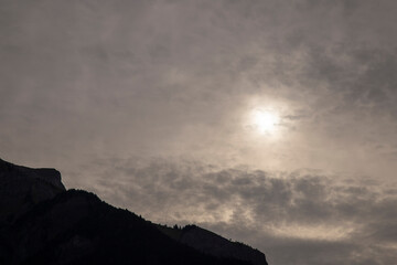 Mountain silhouette with sun behind overcast afternoon sky © Valenti