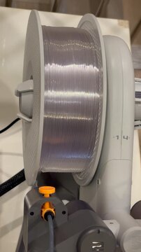 3D Printer filament feeder roll in white, with shiny white filament. In vertical format. 