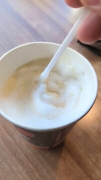 Single-use cup with latte and a plastic stirrer spoon. Represents fast food convenience but highlights excessive plastic consumption and environmental harm.