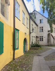 Fototapeta premium Quiet cobblestone lane with a yellow historic building, green shutters and arched doorway in Tallinn Old Town, Estonia.