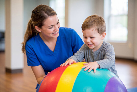 Pediatric Physical Therapist Helping Happy Toddler Boy with Colorful Exercise Ball and Sensory Exercises