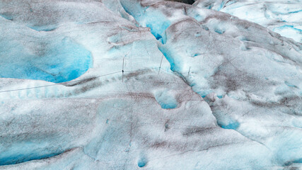 High-angle view of a blue glacier surface in Norway featuring deep crevasses and safety ropes. This image represents climate change, arctic exploration, and environmental preservation efforts. © JULIA