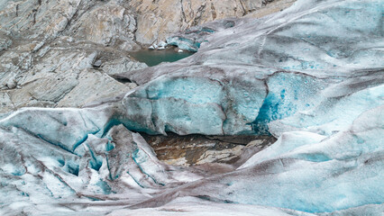 A detailed view of blue glacial ice and deep crevasses in the rugged mountains of Norway. This image represents climate change, environmental sustainability, and the raw power of nature. © JULIA