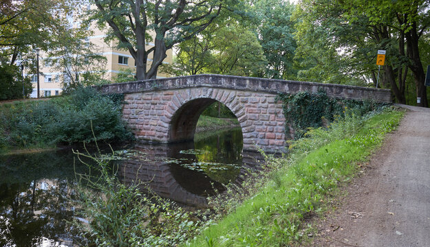 A scenic stone arch bridge crossing a calm canal in a lush green park during the autumn season