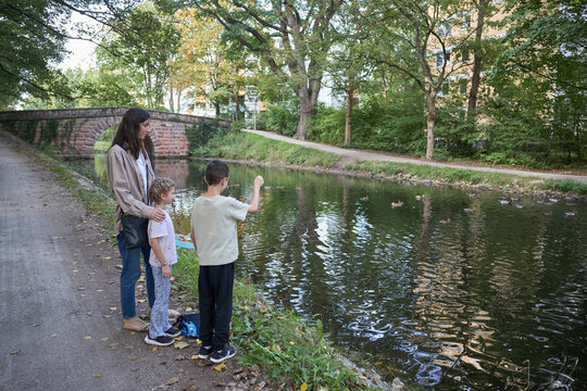 A mother and her two children standing by a canal bank to watch the ducks swimming in the water