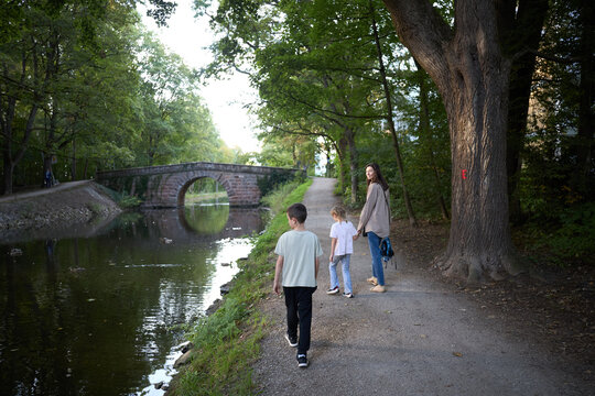 A mother and her two children walking along a peaceful canal path near an old stone bridge