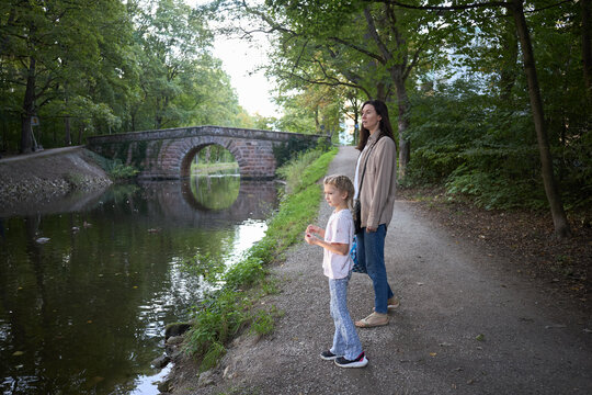 Mother and daughter standing on a peaceful canal path near an old stone bridge in the forest