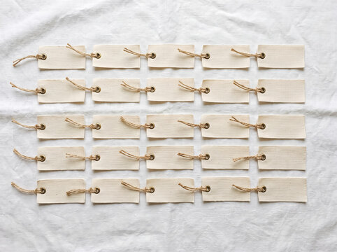 A collection of small, blank tags arranged in neat rows on a white linen background, each with a string tie
