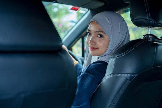 Young woman sitting on a driver's seat in the car and looking at camera over the shoulder