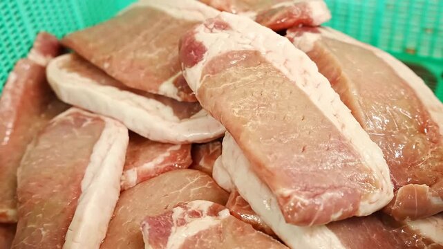 Raw pork meat pieces seasoned with garlic resting inside a green plastic basket before being dipped into a smooth yellow liquid batter inside a metal mixing bowl for culinary preparation