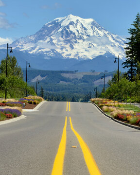 A stunning vertical landscape of a paved road leading the eye toward the majestic, snow-capped peak of Mount Rainier in Washington.