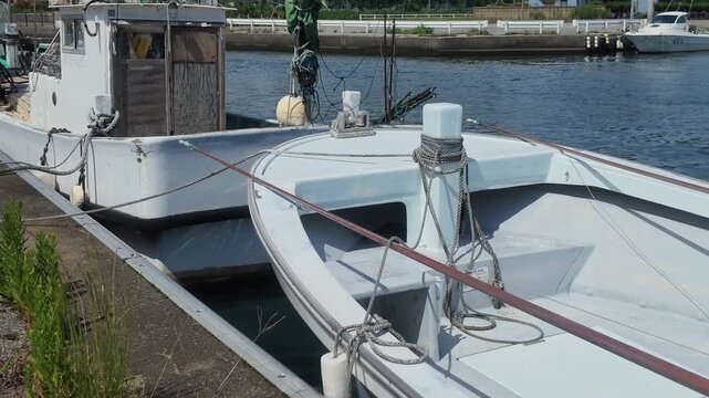 Detailed close-up view of a white fishing boat securely tied with ropes to a bollard at the pier in Kurobe Port, Toyama, Japan. Ideal for maritime, safety, and industry concepts.