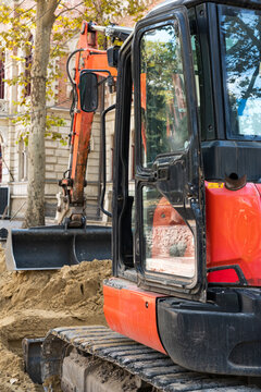 Orange mini excavator digging trench on urban street construction site