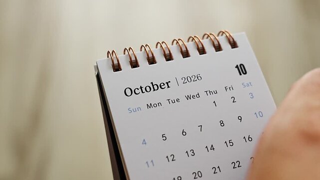 Hand turning desk calendar page from October 2026 to November 2026 against soft neutral background