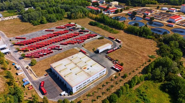 Large transport depot with numerous red city buses. Bus station near waste water treatment plant. Aerial view.
