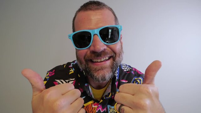 Middle aged man in 1980s graphic pattern shirt neon sunglasses and fanny pack posing humorously trying to look cool on neutral studio background