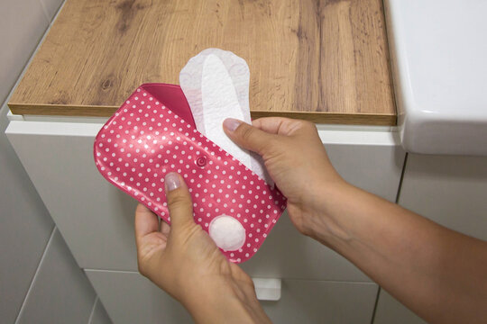 Woman holding pink polka dot feminine hygiene pad package while taking sanitary napkin in bathroom, illustrating menstruation care, personal hygiene, wellness, healthcare, daily routine